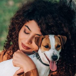 Young woman in raincoat hugging jack russell terrier near tree